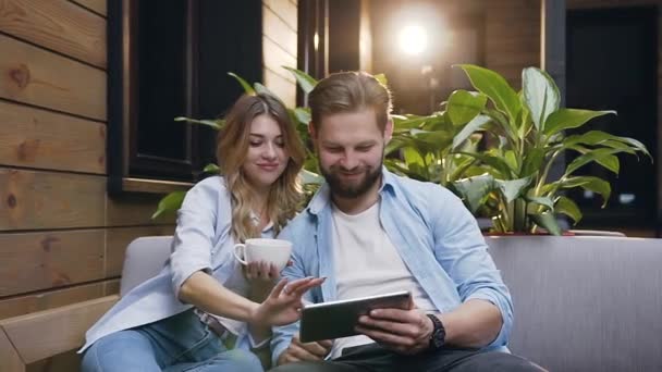 Front view of appealing satisfied cheerful couple of 30s guy and girl which sitting on couch in hotel lobby and using i-pad — Stok video