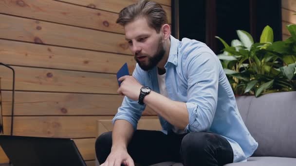 Attractive portrait of bearded young man with passport in his hand which using laptop and happily raised his hands up from seen result on screen while sitting in hall — Stockvideo