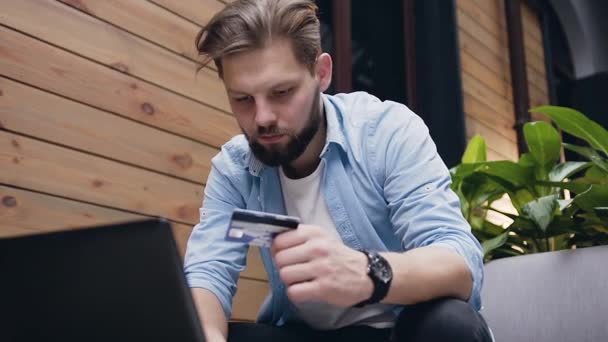 Close view of pleasant confident 30-aged bearded guy which carefully entering the details of his credit card on computer while sitting in hotel lobby — 비디오