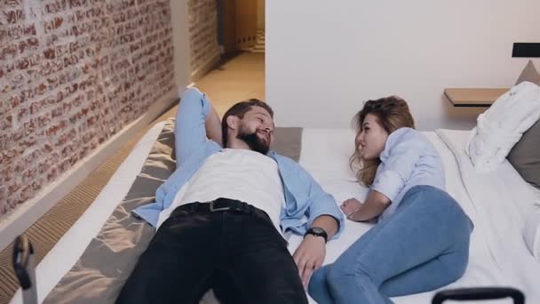 Atractivo retrato de una bonita pareja sonriente feliz que yacía en la cama en la habitación del hotel y hablaba entre sí — Vídeo de stock
