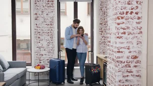 Front view of appealing smiling happy young people in love which standing near window and looking at womans phone — 비디오