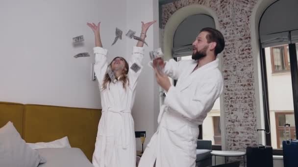 Slow motion of cheerful attractive amorated couple in bathrobes which scattering money in hotel room and happily hugging with each other — Stock Video