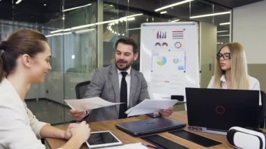Handsome purposeful bearded businessman transmitting for familiarization different reports with graphs to his multiracial male and female partners