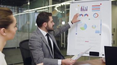 Attractive concentrated multiracial business people sitting at boardroom table and listening the explaination of charts from the serious bearded businessman