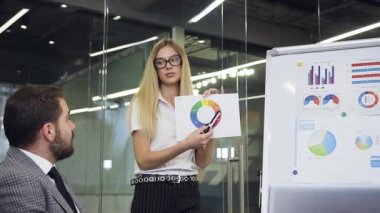 Attractive purposeful blond female corporate worker explaing the graphs about the possible income of company to the good-looking multiracial business colleagues