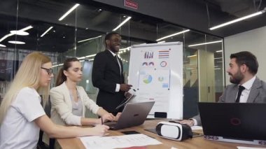 Good-looking black-skinned businessman joking during flip chart presentation with pleasant smiling business partners