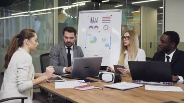 Attractive multiracial two businessmen and two beautiful smiling businesswomen sitting together at the meeting table and working under joint project