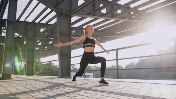 Young happy sporty girl in black top and leggings doing fitness exercises outdoors — ストック動画