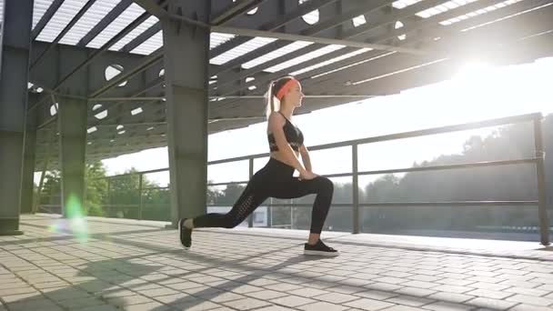 Attraente donna atletica sorridente in abiti da fitness che fa esercizi di stretching in terra all'aperto — Video Stock