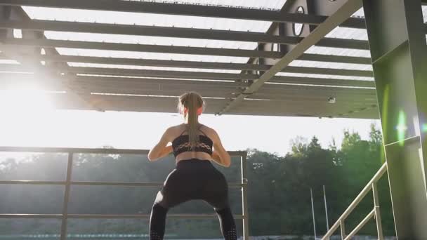 Back view of sexy slender young woman in fitness clothes which doing squat exercises outdoors under roof — 图库视频影像