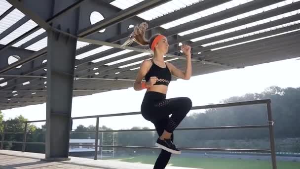 Jovem atlética flexível em roupas fitness correndo no local durante seu treinamento ao ar livre — Vídeo de Stock