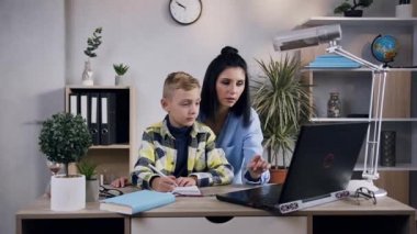 Front view of appealing dark hair 35-aged woman which working together with her handsome little boy at the computer