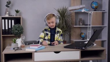 Lovely happy teen boy in headphones listening music and playing on computer in his room