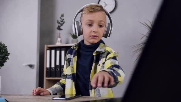 Ελκυστικό μικρό χαρούμενο αγόρι σε ακουστικά κινείται το σώμα του κάτω από δροσερή μουσική στο σπίτι — Αρχείο Βίντεο