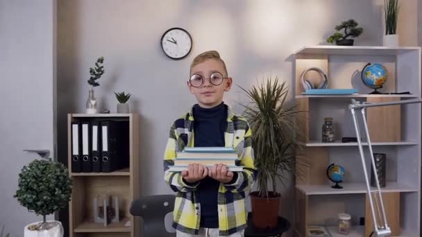 Close view of attractive satisfied little schoolboy which holding on hands his books and looking at camera at home — 비디오