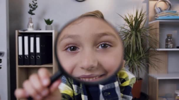Hezký úsměv dospívající chlapec dívá přes lupu doma — Stock video