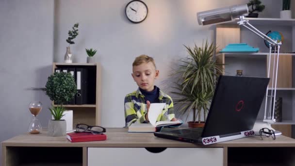 Привлекательный умный современный мальчик читает книгу за столом дома — стоковое видео