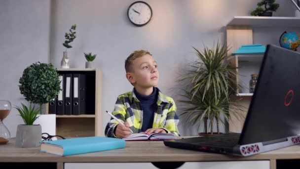 Thoughtful attractive modern boy in plaid shirt sitting at the table and writing notes into the diary — Stock Video