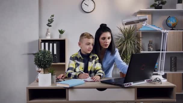 Aantrekkelijk portret van charmante brunette vrouw die zitten aan de tafel met haar tienerzoon en werken met de computer — Stockvideo