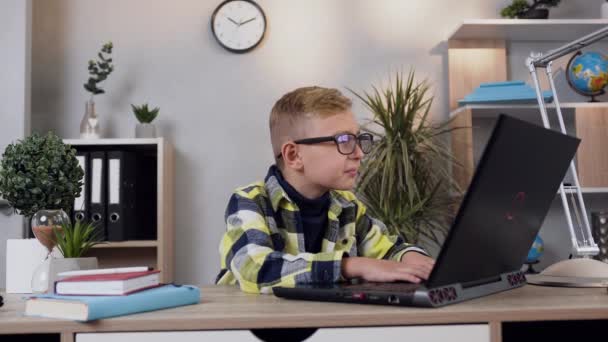 Front view of likable smart modern teen schoolboy in glasses which sitting at the computer at home — 비디오