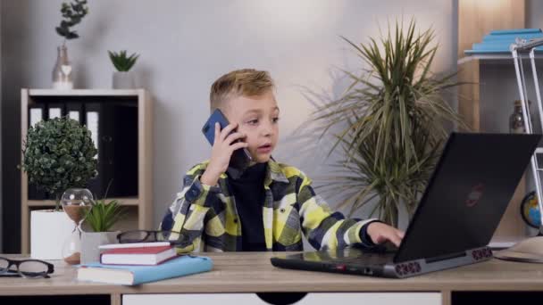 Slow motion of handsome smart modern teen boy which working at computer and talking on phone with friend — Stok video