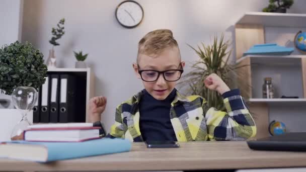 Framifrån av glad glad glad blond pojke i glasögon som höjde händerna upp från goda nyheter på telefonskärmen — Stockvideo