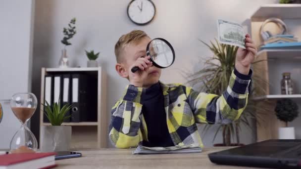 Ganteng pintar anak remaja memegang di tangannya dolar uang kertas dan memeriksa melalui pembesar di rumah — Stok Video