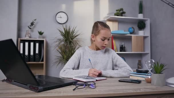 Elölnézetben vonzó világos haj tini lány modish pulóver, amely befejezte, hogy írjon a notebook és felveszi a szemüvegét — Stock videók