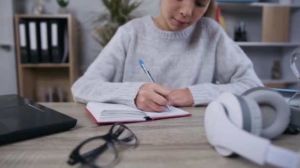 Front view of concentrated appealing 15-aged schoolgirl in gray knitted sweater which writing out from laptop the notes into her diary — Stock Video