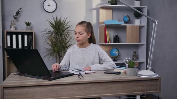 Портрет задоволеної милої дівчини-підлітка, що працює під домашнім столом за допомогою комп'ютера та приватного блокнота — стокове відео