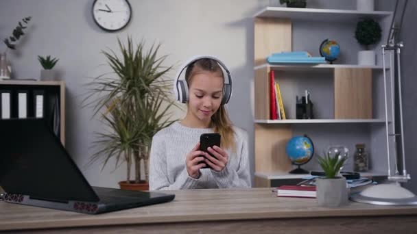 Satisfait souriant jeune fille moderne dans les écouteurs écoutant de la musique en utilisant la playlist de son mobile — Video