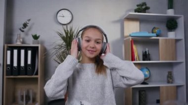 Çekici, neşeli, gülümseyen genç kız kulaklıkla müzik dinlerken kameraya bakıyor.