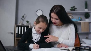 Close up of insistant good-looking brunette woman which controling how her 10-aged cute daughter doing hometask
