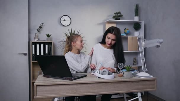 Attraktive brünette Mutter schreibt in das Notizbuch, während ihre lächelnde Tochter mit dem Computer arbeitet und Mutter um Hilfe bittet — Stockvideo