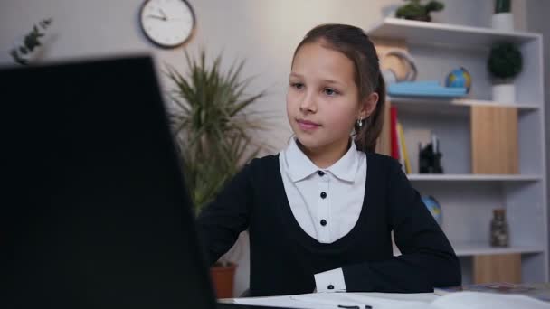 Gros plan d "écolière primaire souriante heureuse qui lit sur l" écran de l'ordinateur portable et écrit une œuvre dans le copybook — Video