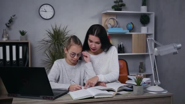 Koncepcja edukacji rodzinnej, gdzie piękna brunetka pomaga jej inteligentny nastolatek córka w okularach zrobić hometask — Wideo stockowe