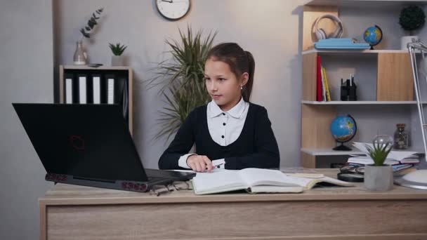Első látásra mosolyog boldog iskolás lány egyenruhában, amely ül a munkahelyén, és csinál otthoni számítógépes — Stock videók