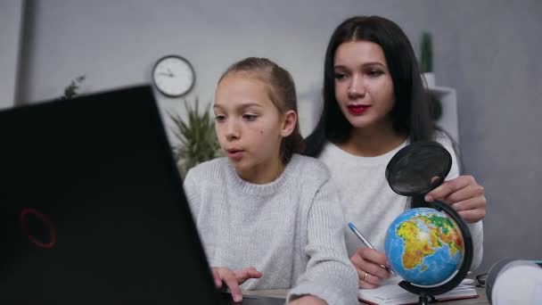 Nahaufnahme von gut aussehenden selbstbewussten, fleißigen Mutter und Teenager-Mädchen, die zusammen Geografie-Aufgabe am Computer mit Lupe und kleiner Weltkugel erledigen — Stockvideo