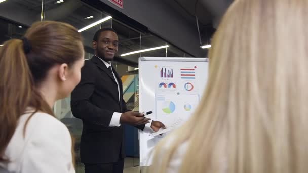 Zeitlupe zielstrebiger gut aussehender Geschäftsfrauen, die dem lächelnden gutaussehenden Geschäftsmann während der Flipchart-Präsentation verschiedene Fragen stellen — Stockvideo