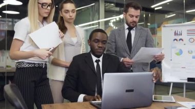 Front view of the clever experienced african american businessman which showing to his considerate purposeful male and female business colleagues the computer business plan