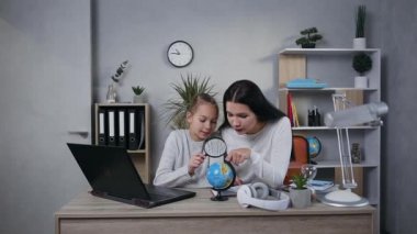 Attractive happy smiling mother and teenage daughter looking on small globe through the magnifier at home