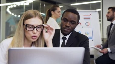 Business concept where two concentrated industrious mixed race businees people which working with computer in meeting room together with another members of their group