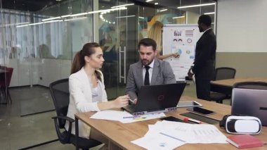 Close up of attractive serious high-skilled multiethnic business colleagues which working at the meeting table using computer and flip chart board