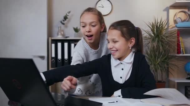 Frontansicht von zwei fröhlich lächelnden sympathischen Teenie-Mädchen, die während ihrer Hausaufgaben den Computer benutzen — Stockvideo