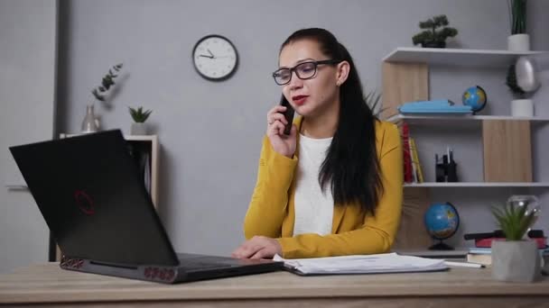 Rust vol vertrouwen hoog opgeleide volwassen zakenvrouw in bril gekleed in trendy jas praten op de telefoon tijdens het werken op laptop — Stockvideo