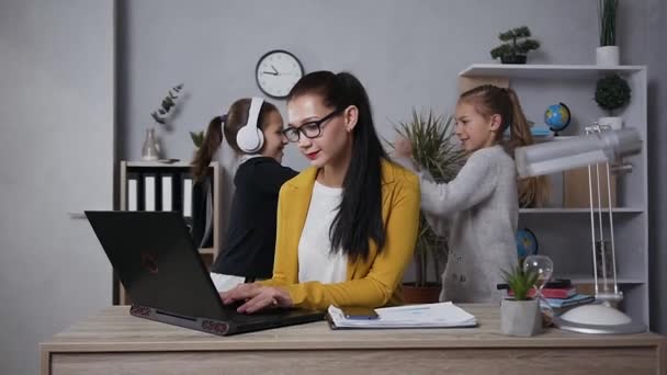 Müde konzentrierte hübsche brünette Geschäftsfrau mit Brille massiert die Schläfen, weil ihre lärmenden verspielten Teenie-Töchter ihre Arbeit zu Hause stören — Stockvideo