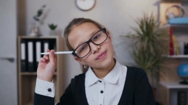 Okul üniformalı 10 yaşında bir kız dersini alırken başını kaldırmıyor ve kameraya samimi bir gülümsemeyle bakıyor.