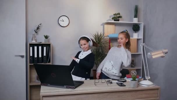 Закройте улыбающихся веселых двух девочек-подростков, которые делают танцевальные движения, которые показывают на экране компьютера — стоковое видео