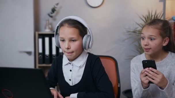 Привлекательный портрет увлекательных девочек-подростков, которые веселятся вместе во время игры с помощью ноутбука и телефона — стоковое видео