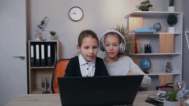 Вид спереду дружні задоволені дівчата-підлітки, які сидять за столом і грають в онлайн відеогру на ноутбуці — стокове відео